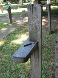 A knife lays on the upper flat surface of a wooden cross grave marker.