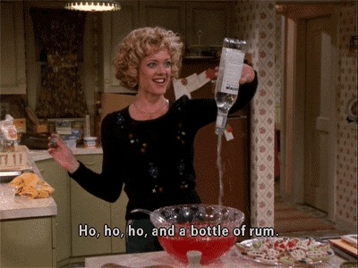 A white woman with blonde curly hair in a sparkly black dress upends a bottle of clear rum and empties it into a punchbowl. The subtitle reads: "Ho, ho, ho, and a bottle of rum!"