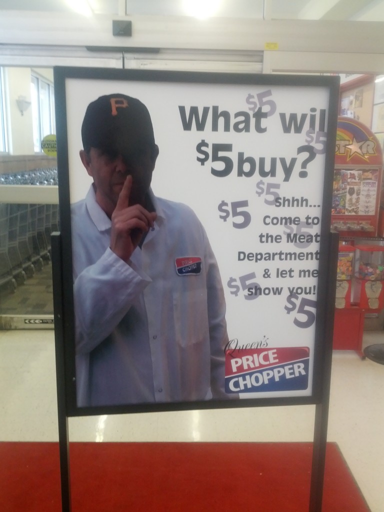 A grocery store ad. A light-skinned man in a white lab coat and a baseball cap holds a finger to his lips. The text reads, "What will $5 buy? Shhh...come to the meat department and find out."