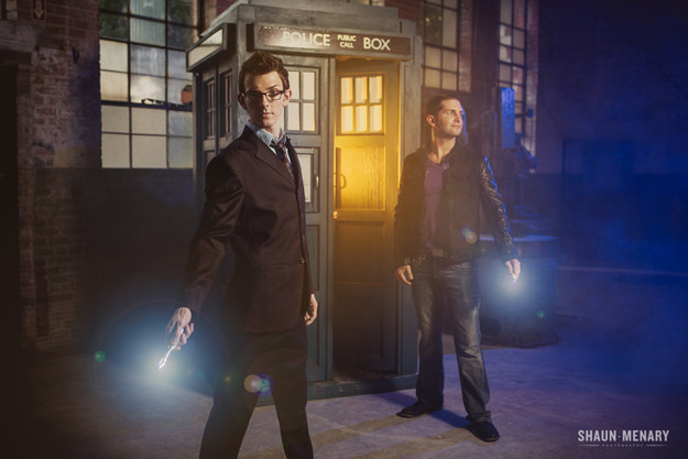 Two white men,, one dressed in a suit like the Tenth Doctor and one dressed in jeans, tshirt and leather jacket like the Ninth Doctor, pose in front of a TARDIS while holding sonic screwdrivers.