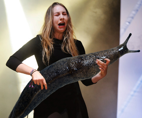 White woman Este Haim makes what looks like a disgusted face at the giant slug that was photoshopped into the photo where her bass guitar would be.