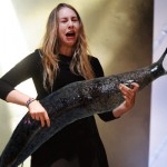 White woman Este Haim makes what looks like a disgusted face at the giant slug that was photoshopped into the photo where her bass guitar would be.