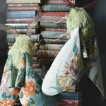 Fuzzy green moths with wings made from vintage needlepoint tapestry climb a set of 19th century books.